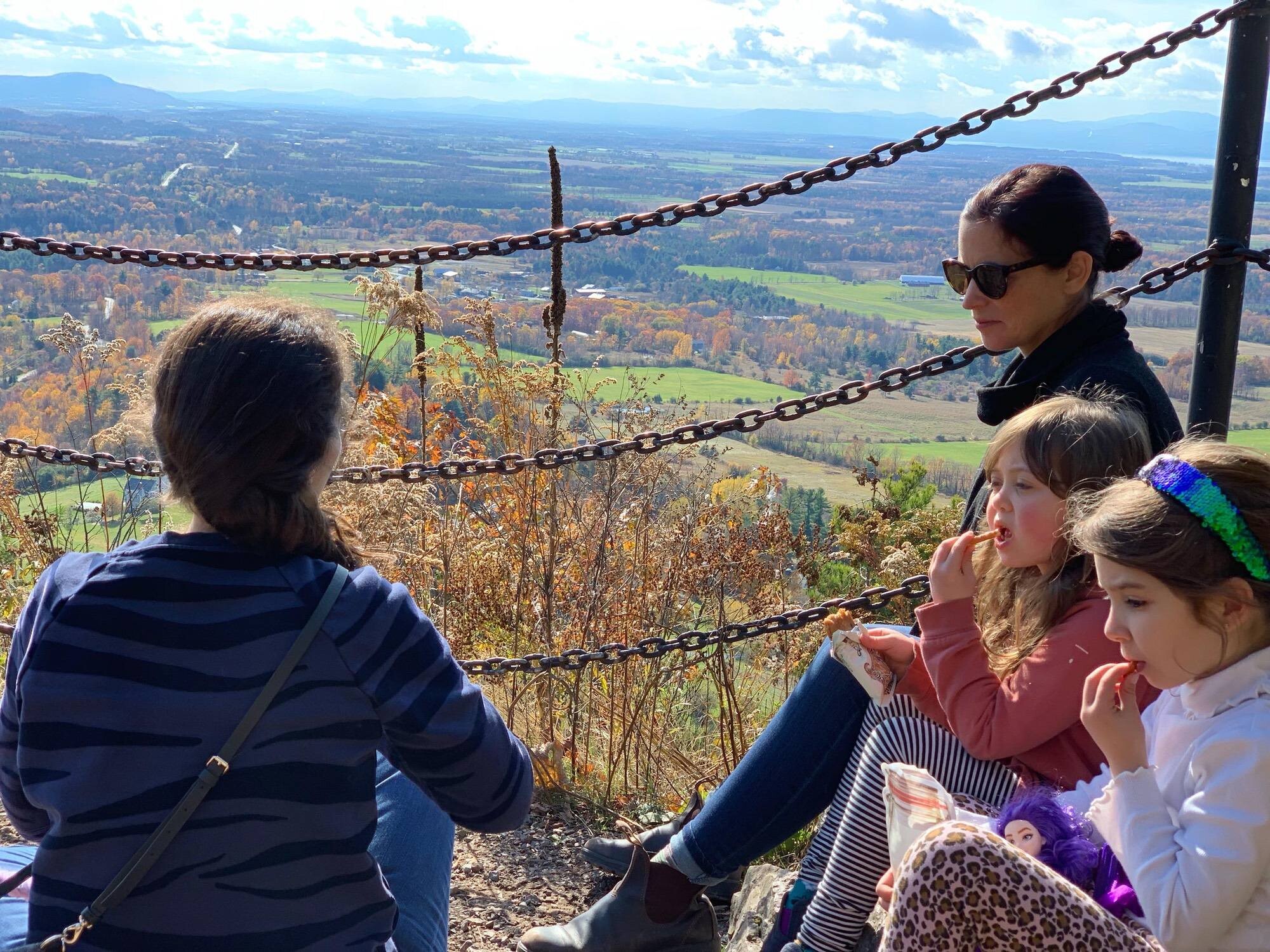 Moms sitting with two young girls overlooking Vermont foliage scene