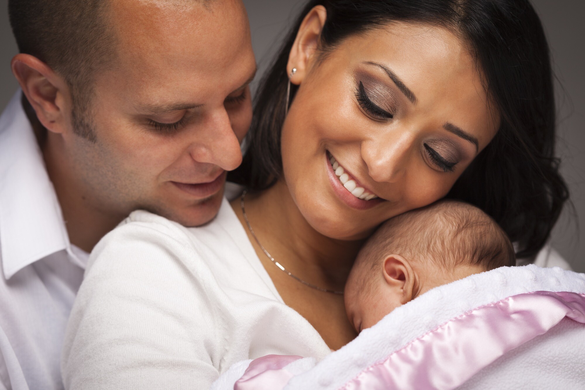 Man and woman smiling at the sleeping infant in their arms