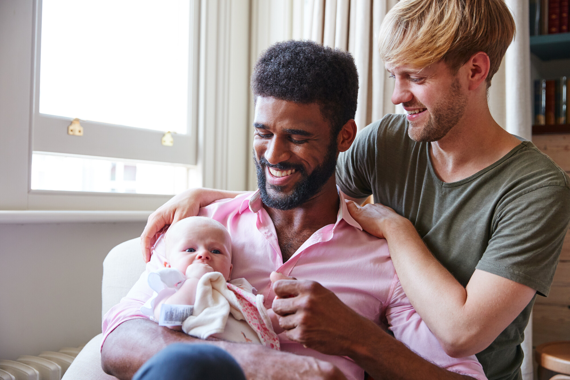 Loving Male Couple Cuddling Baby Daughter On Sofa at Home