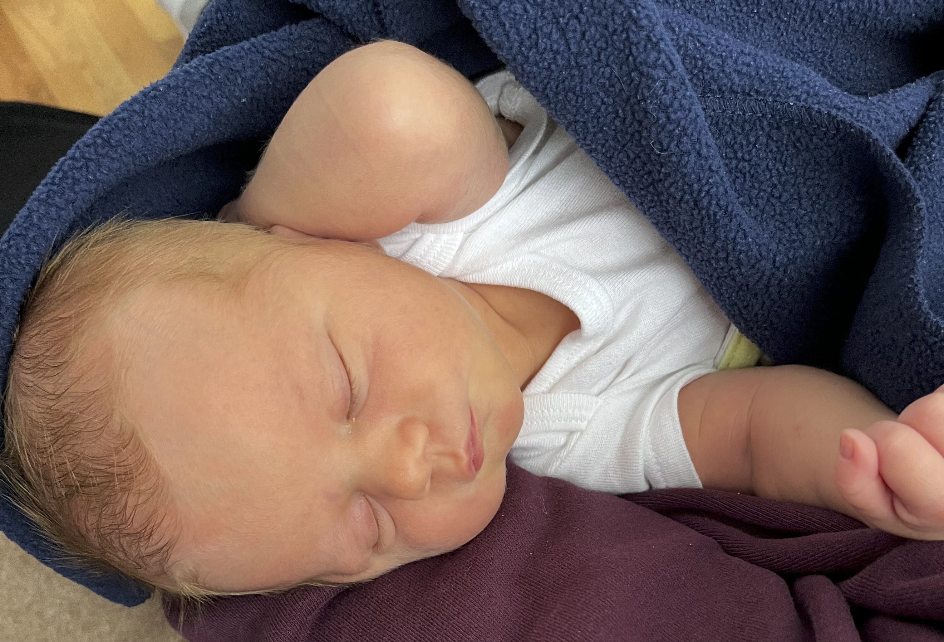 Close up of a sleeping infant swaddled in a blue blanket.