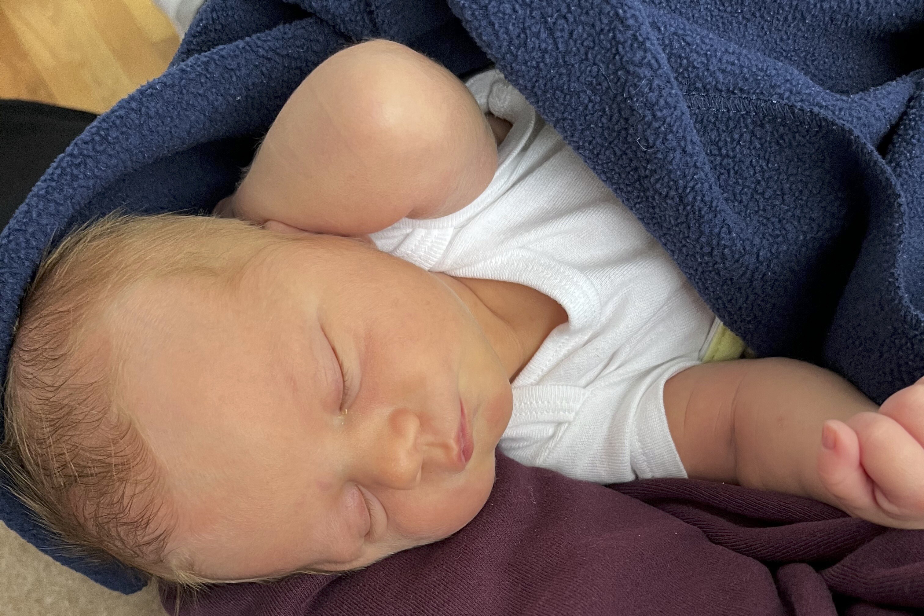 Close up of a sleeping infant swaddled in a blue blanket.