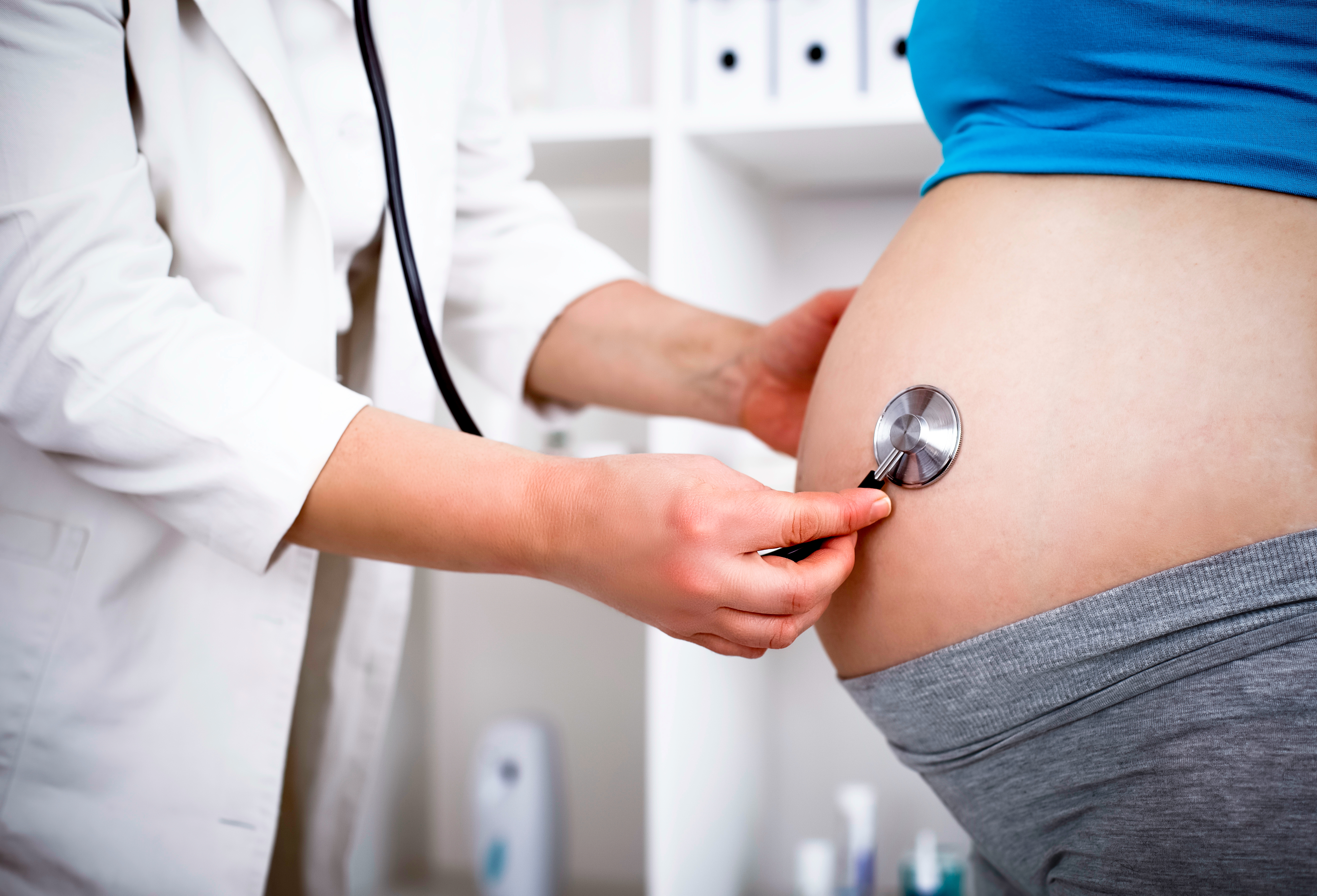 doctor holding stethoscope on pregnant woman's belly